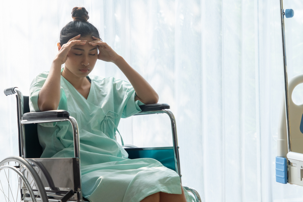 A female patient siting in a wheelchair holding her head in discomfort