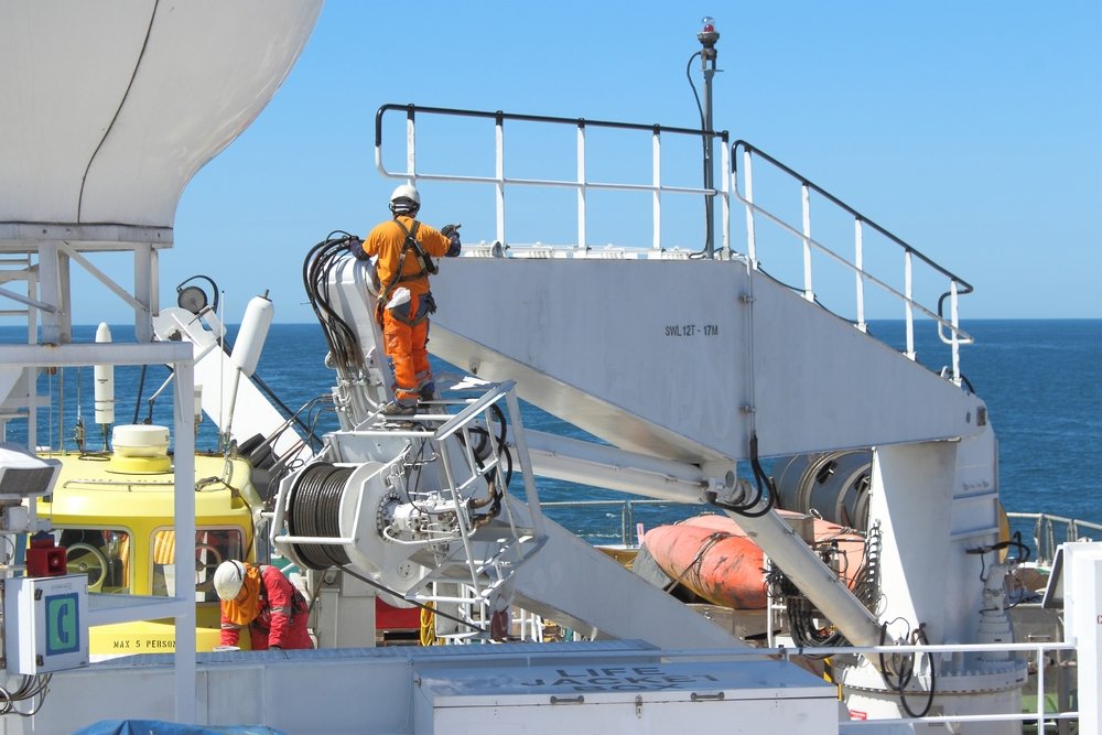 Worker in orange PPE inspects crane equipment on an offshore vessel deck, highlighting maritime injuries risks during ship operations